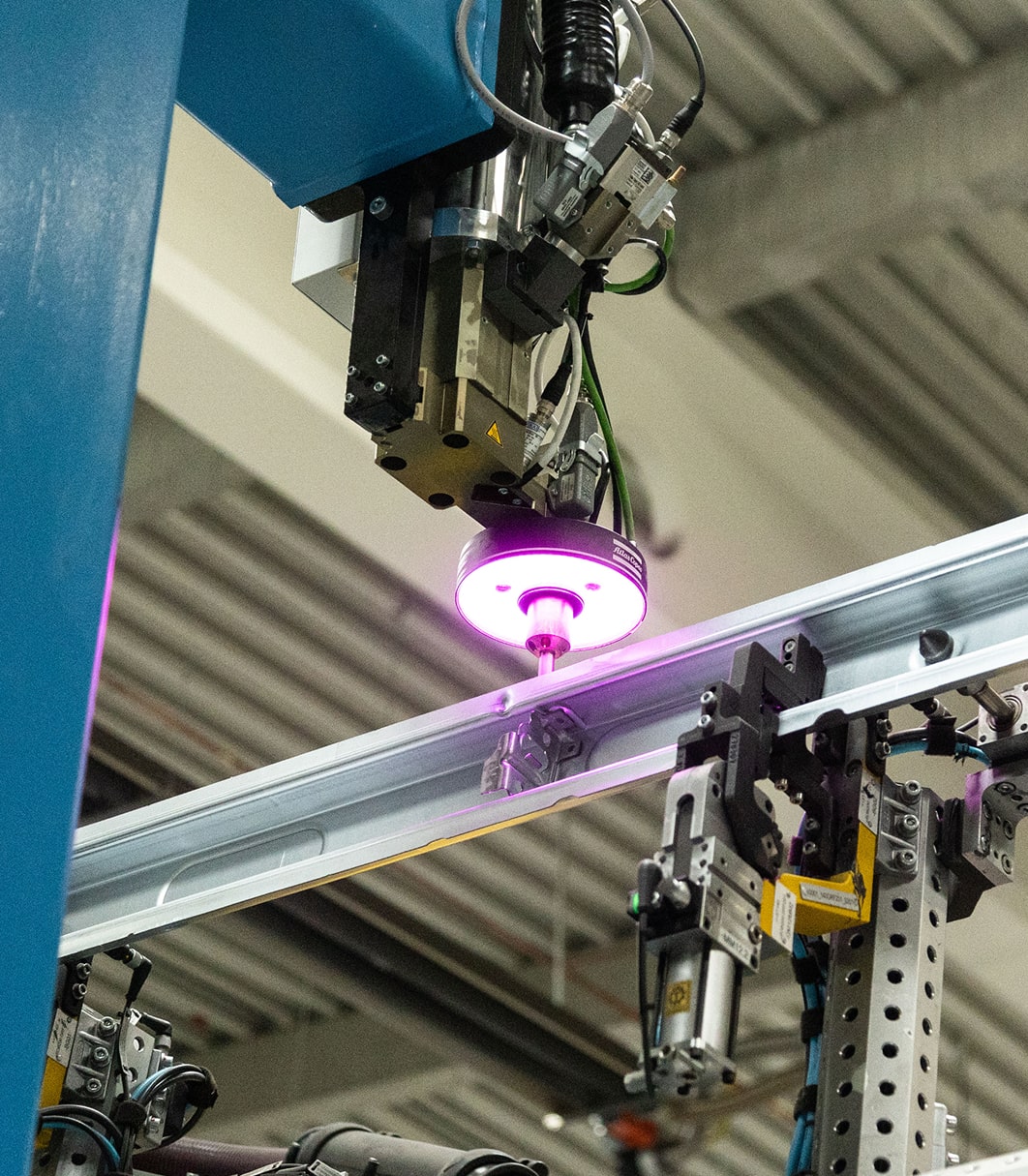 Industrieroboter mit pinkem Lichtstrahl beim präzisen Fügen eines Metallbauteils.
