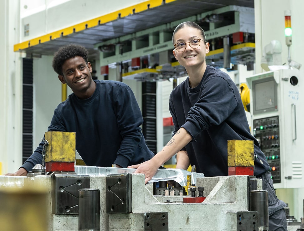 Zwei junge Auszubildenden arbeiten in einer Industriehalle.