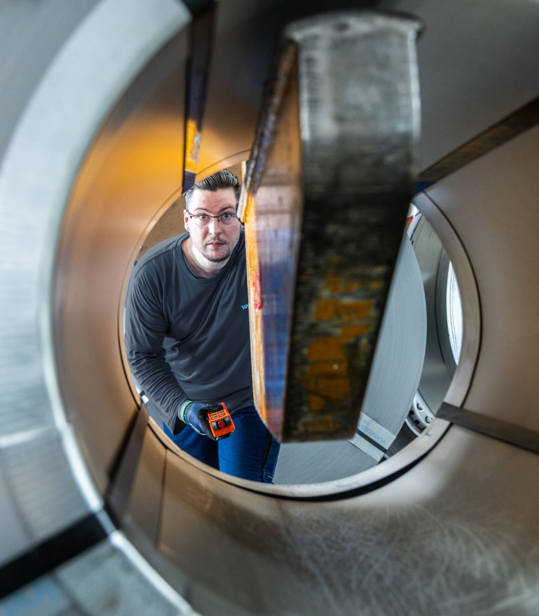 Ein Mitarbeiter von Sungwoo Hitech blickt durch einen großen Stahl-Coil und prüft das Material.